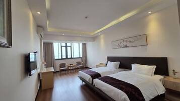 A hotel room with two beds, a desk, a chair, a TV, and a window.