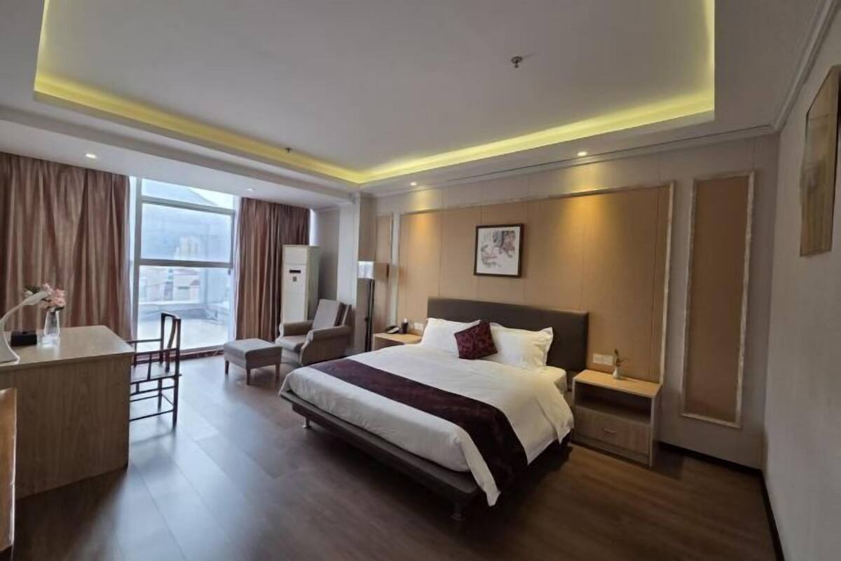 A modern hotel room with a large bed, bedside tables, a desk with a chair, and a view of the city.
