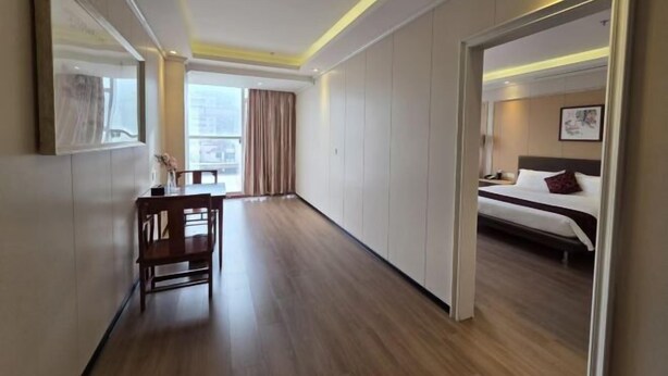 Ein Hotelzimmer mit Bett, Schreibtisch und Stuhl. Ein Fenster mit Vorhängen, und der Boden ist mit Holz ausgelegt.