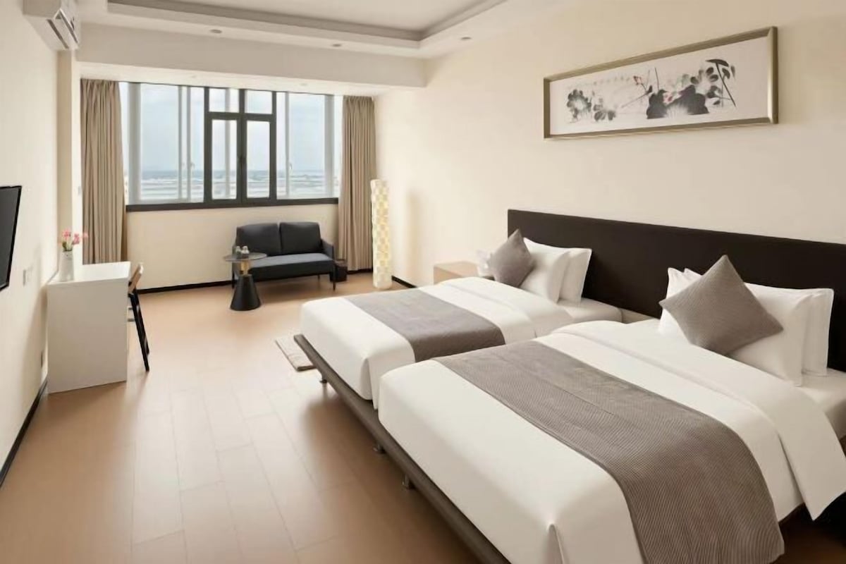 Une chambre d’hôtel avec deux lits, un canapé, un bureau et une grande fenêtre donnant sur un beau paysage.