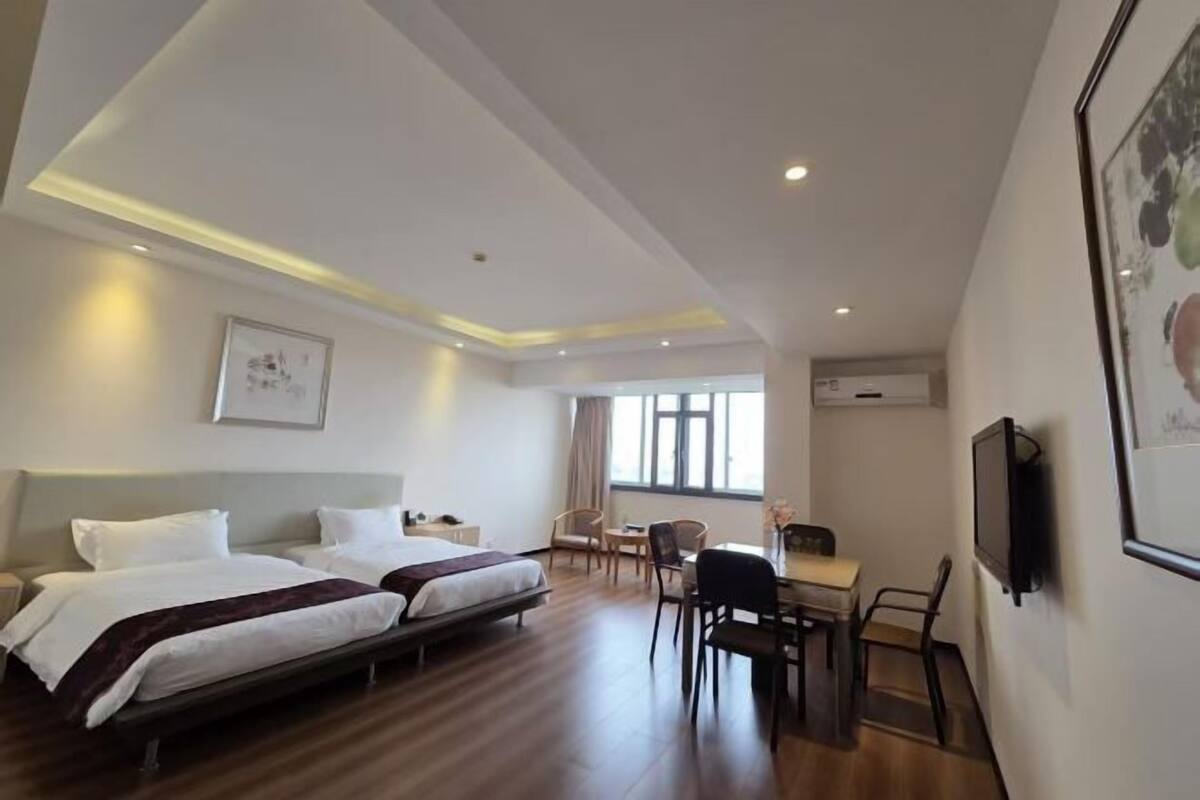 A hotel room with two beds, a desk, chairs, a TV, and a window.