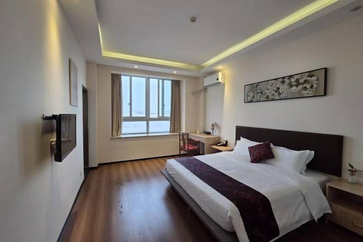 A hotel room with a bed, desk, chair, and artwork on the wall.