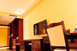 A hotel room with a wooden desk, a chair, a television mounted on the wall, and a water bottle on the table. - Xingdu Hotel (Fangchenggang)