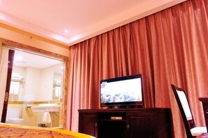 A hotel room with a television on a wooden stand, a large mirror, and a view of the bathroom. - Xingdu Hotel (Fangchenggang)