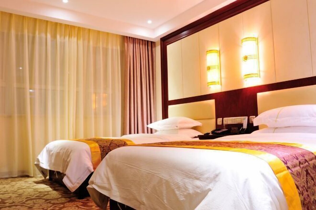 A hotel room with two beds, a large mirror, and wall sconces.