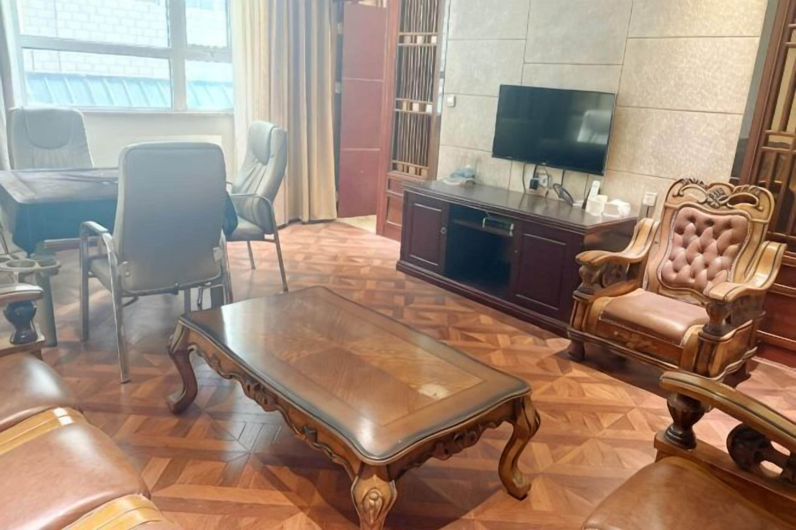 A room with a wooden parquet floor, a television on a stand, a sofa, a chair, and a cabinet.