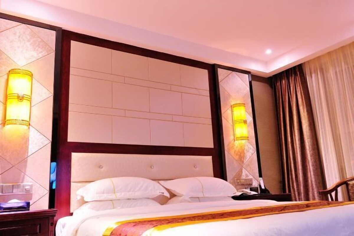 A hotel room with a large bed, a wooden headboard, and two wall-mounted lamps.