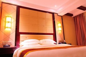 A hotel room with a large bed, a headboard with a wooden frame, two bedside lamps, and a nightstand.