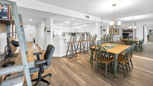 Eine moderne Küche mit weißen Schränken, ein Essbereich mit Holztischen und -stühlen sowie ein Arbeitsbereich mit Schreibtisch und Stuhl.