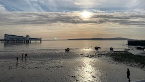 Una playa con muelle, agua tranquila y un atardecer.