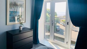 Una habitación con un ventanal grande, un aparador oscuro, un cuadro en la pared y una planta en maceta sobre el aparador.