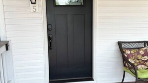 Une porte d’entrée noire avec une fenêtre au-dessus, une boîte aux lettres et un paillasson sur un porche.