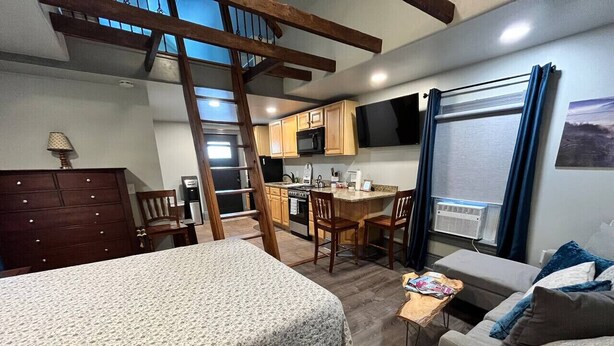 Une pièce confortable comprenant un lit, un canapé, une commode en bois, un bureau avec une lampe et un coin cuisine avec des placards en bois et un four à micro-ondes.