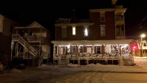 Un bâtiment à deux étages doté d’un porche décoré de guirlandes lumineuses et de festons, le tout entouré de neige.