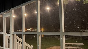 A glass-enclosed room with a view of a sandy area and a bench. - Waterfront Harbor Home, Sunset Views, Fireplace, Private dock and Boat Slip (Kill Devil Hills)