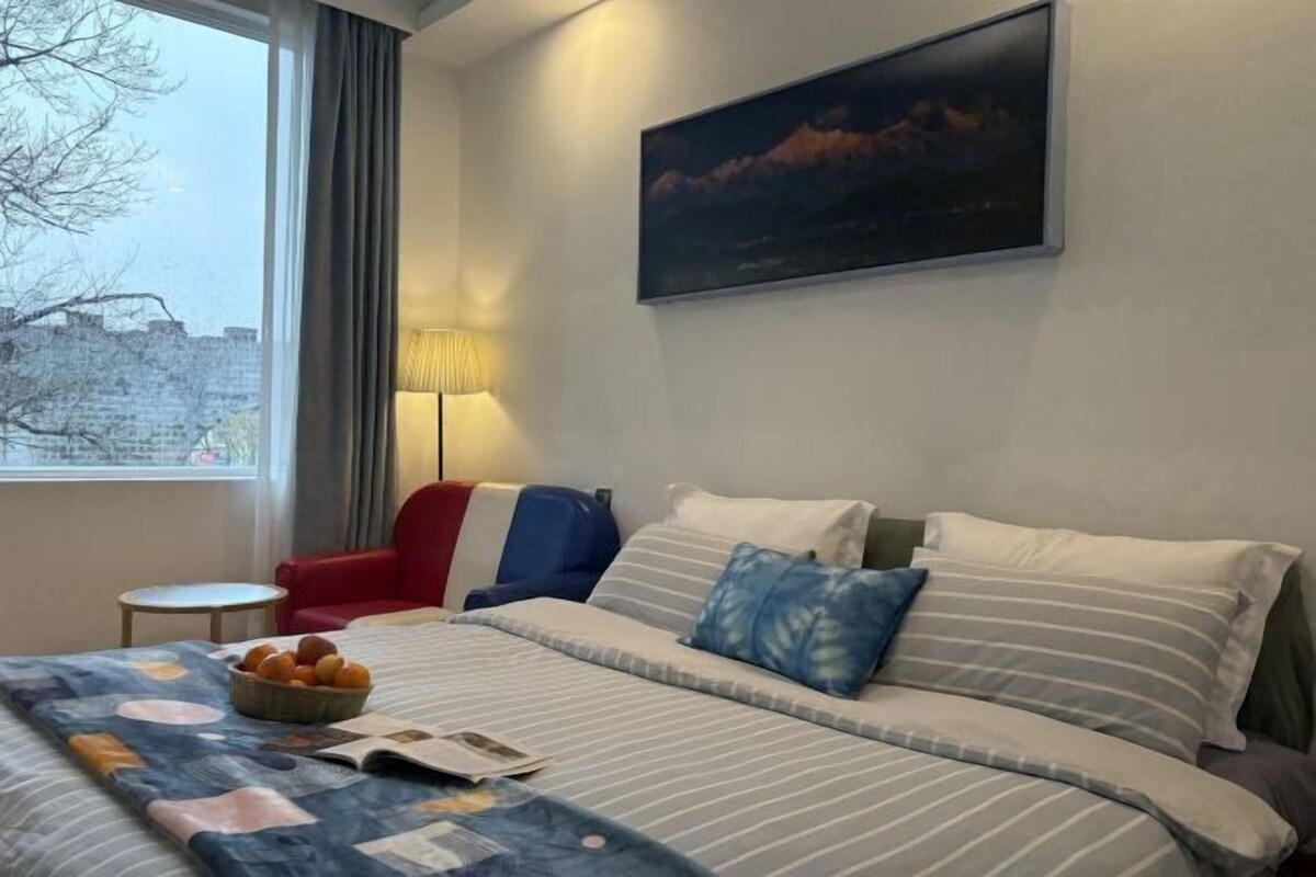 A hotel room with a bed, a red chair, a lamp, and a painting on the wall.