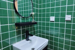 A bathroom with a white sink, black faucet, and a mirror above it. The walls are covered with green tiles. - V-Hostel (Dali City)