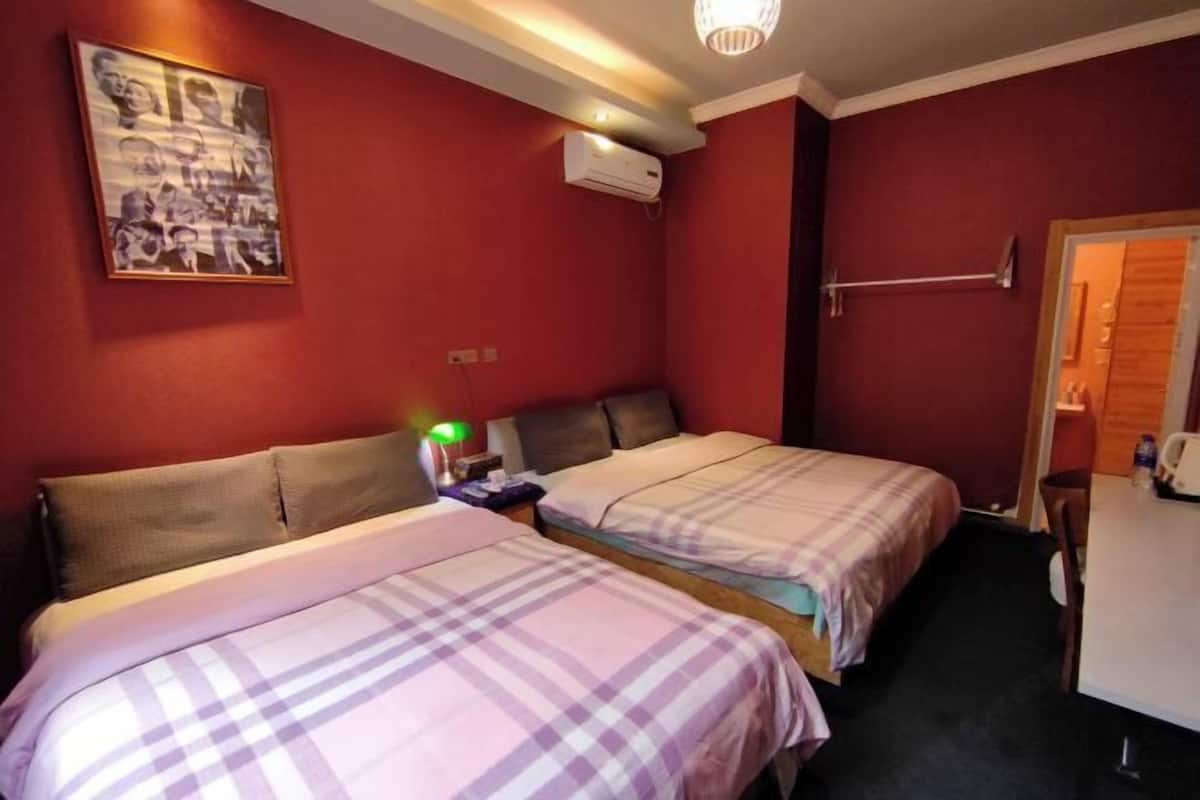 A hotel room with two beds, a desk, a chair, a wall-mounted air conditioner, and a painting.