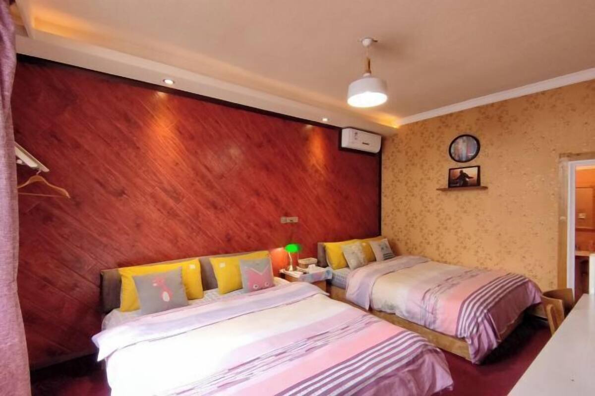 A bedroom with two beds, wooden walls, a clock, and a small table with a lamp.