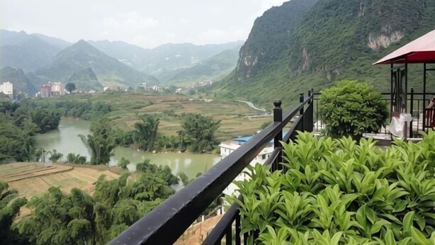 A river valley with mountains, a bridge, and a building with a red roof.