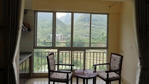 A balcony with a view of green hills and buildings, two chairs, and a small table.