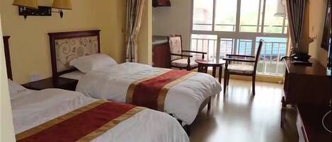 A hotel room with two beds, a chair, a desk, and a window with a view.