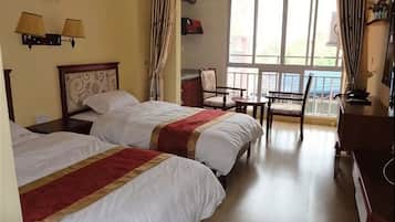 A hotel room with two beds, a desk, a chair, and a large window.