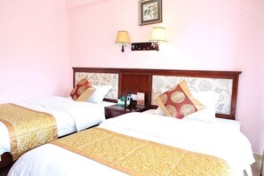 Quarto de hotel com duas camas, uma mesinha de cabeceira e uma luminária fixada na parede.