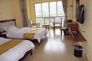 Quarto de hotel com duas camas, uma escrivaninha, uma cadeira, uma televisão e uma varanda com cortinas.