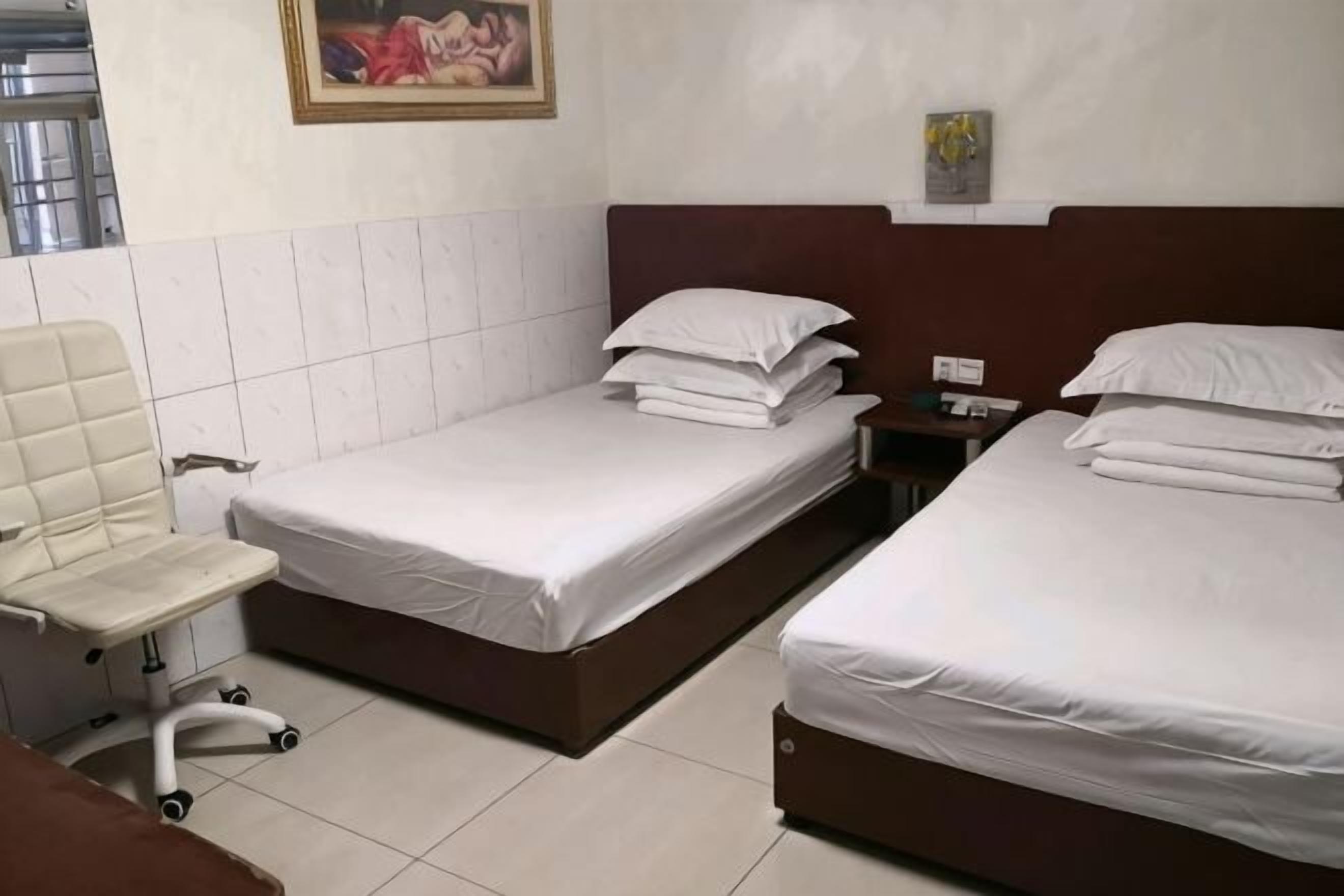 Ein Hotelzimmer mit zwei Betten, einem Sessel, einem Nachttisch und einem Bild an der Wand.