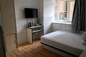 A small room with a bed, a desk, a TV, and a window with curtains.