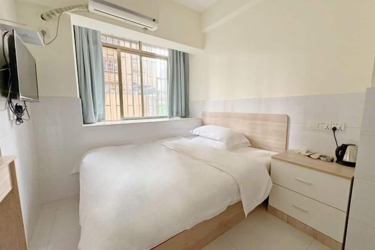 A hotel room with a bed, a bedside table, a TV, and a window with curtains.