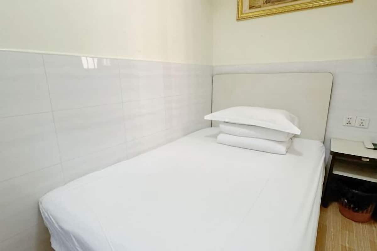 A small, neatly made bed with white bedding in a room with white tiled walls and a simple headboard.