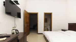 Hotelkamer met een bed, een bureau met waterkoker, een aan de muur bevestigde televisie en twee deuren naar andere kamers.