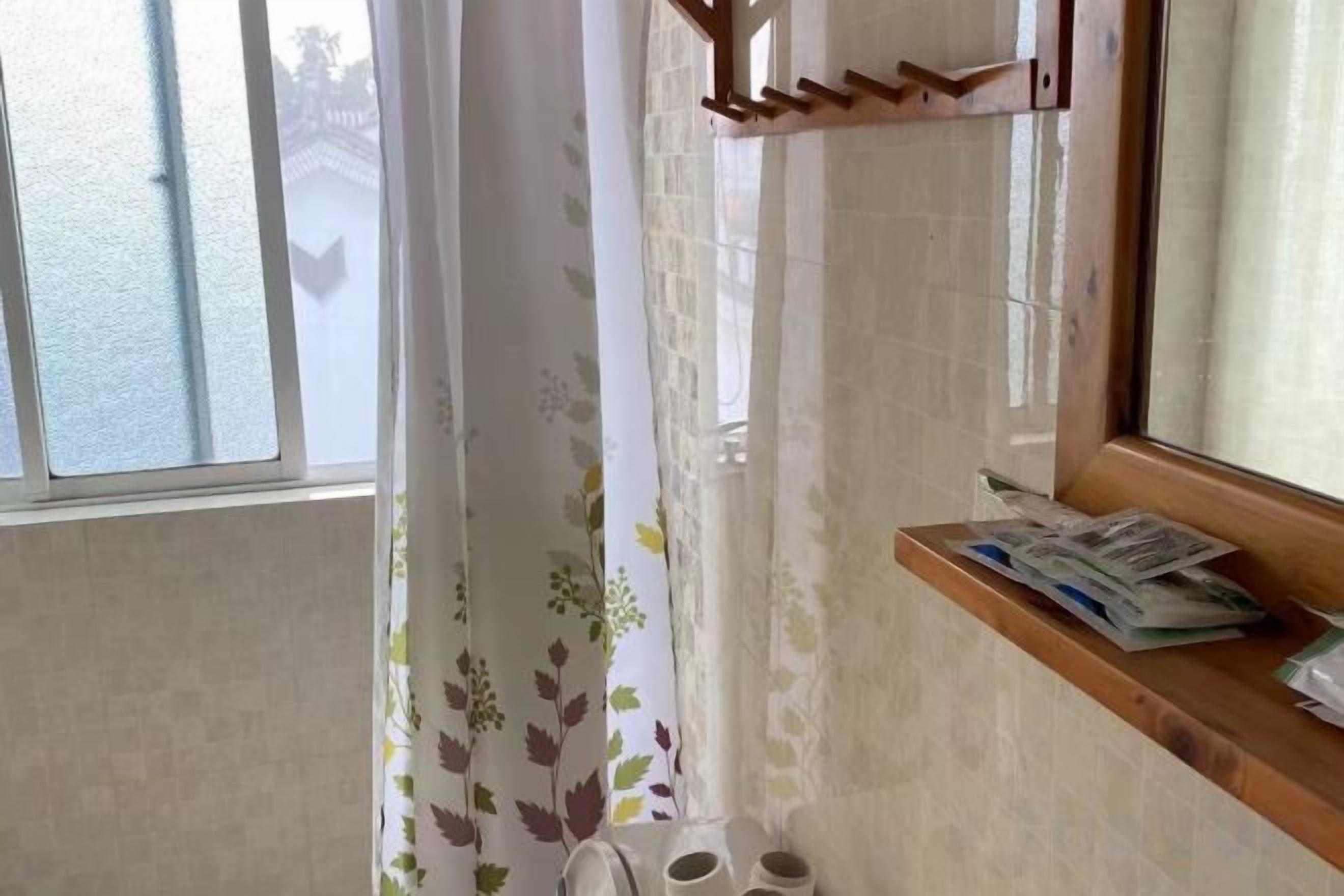 Un baño con ventana, cortina de ducha, estante con periódicos y un perchero.