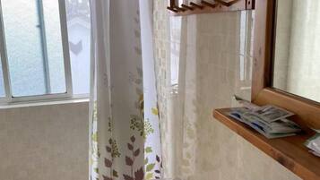 Un baño con ventana, cortina de ducha, estante con periódicos y un perchero.