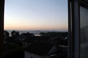 Blick aus einem Fenster auf ein Wohngebiet mit traditioneller Architektur und ein Gewässer in der Ferne.