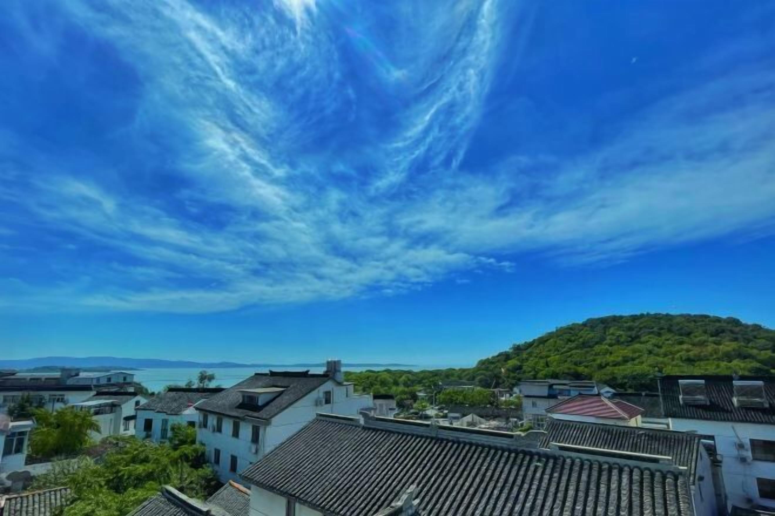A coastal town with traditional buildings, a hill with greenery, and a clear blue sky.
