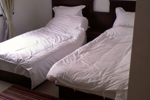 Una habitación con dos camas individuales, cabecero de madera, alfombra a rayas y una ventana con cortinas.