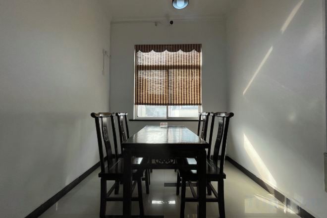 Un comedor con una mesa rectangular y cuatro sillas, una ventana con persianas y una lámpara en el techo.