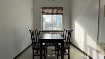 A dining area with a rectangular table and six chairs, a window with a striped valance, and a door on the right.