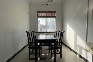 Un coin repas avec une table rectangulaire et six chaises, une fenêtre agrémentée d’une lambrequin à rayures et une porte située à droite.