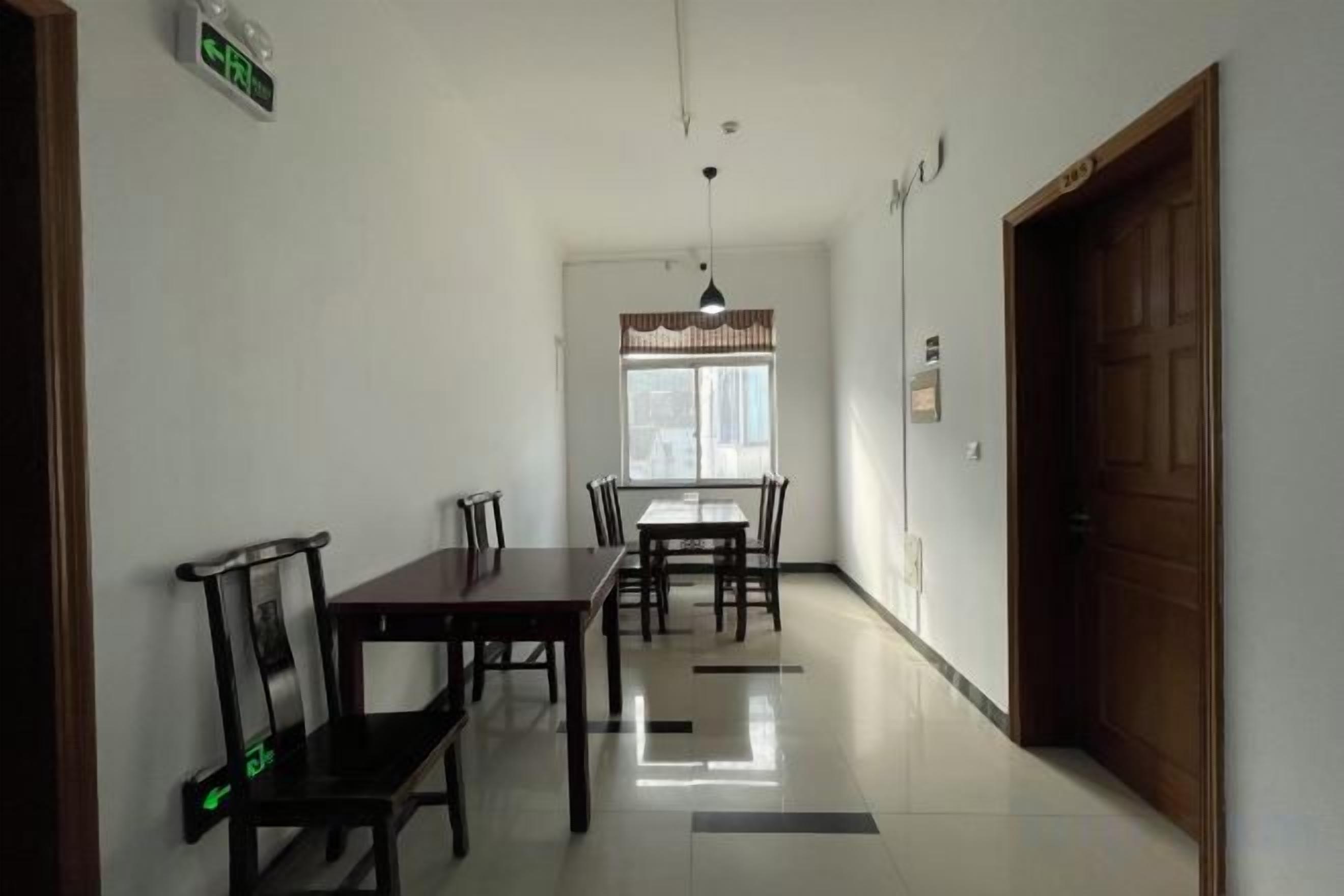 A hallway with a dining area featuring a table and chairs, a wooden door, and a window with a curtain.