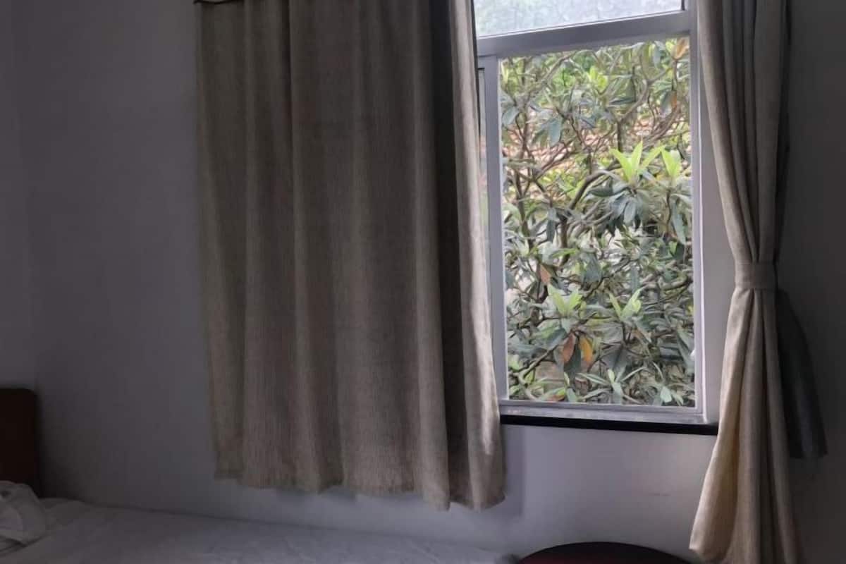 Ein Zimmer mit einem Bett, einem Vorhangfenster und Blick auf Grünfläche.
