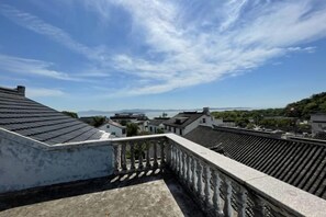 Une terrasse sur le toit, dotée d’une balustrade, qui offre une vue sur une ville aux bâtiments traditionnels et un ciel dégagé.