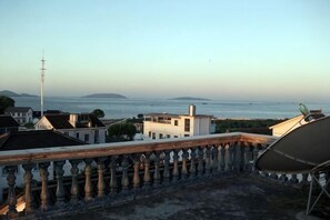 Un balcón con barandilla, una antena parabólica y vistas al mar y la costa distante.