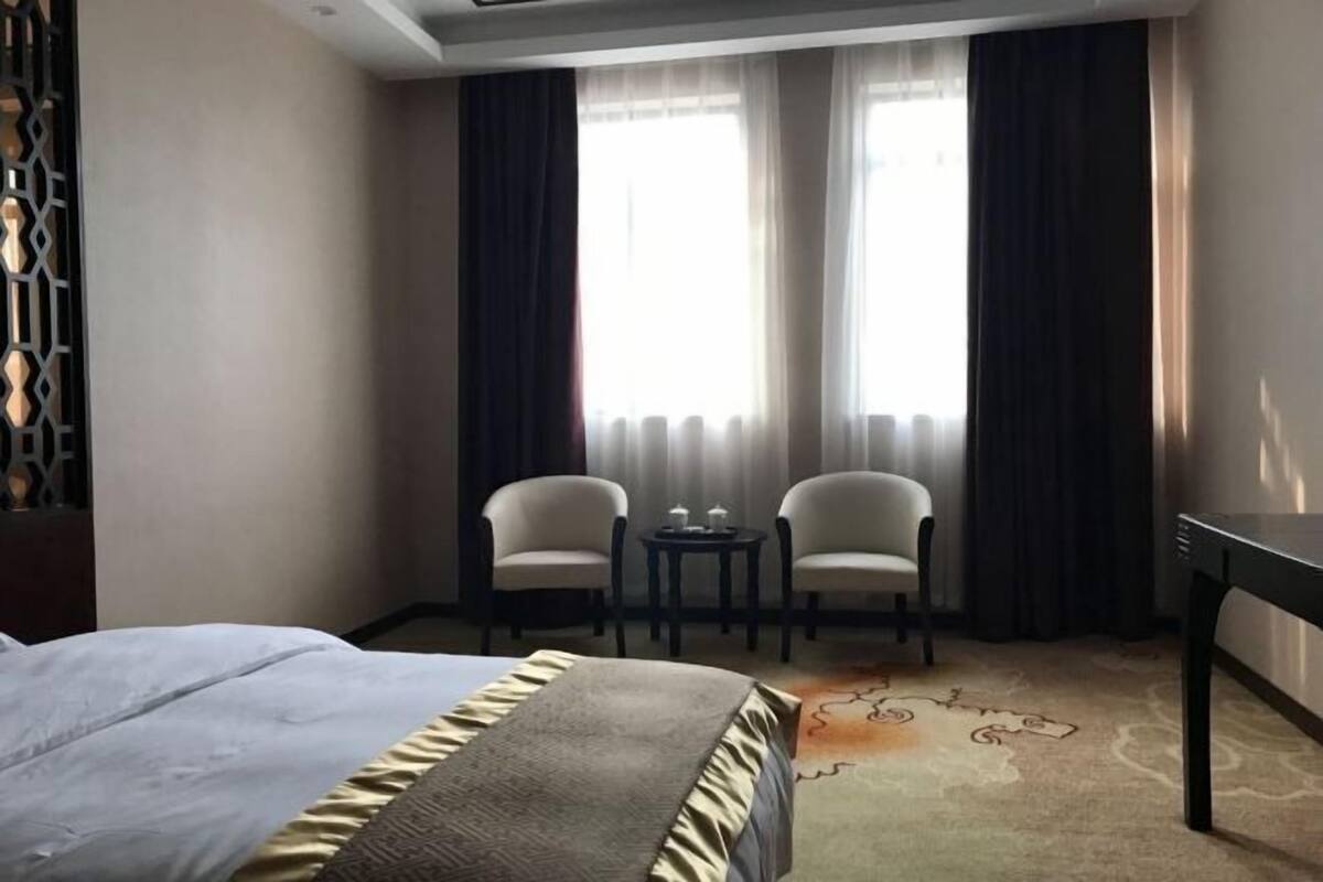 A hotel room with a bed, two chairs, a small table, and a view of the outdoors through large windows.