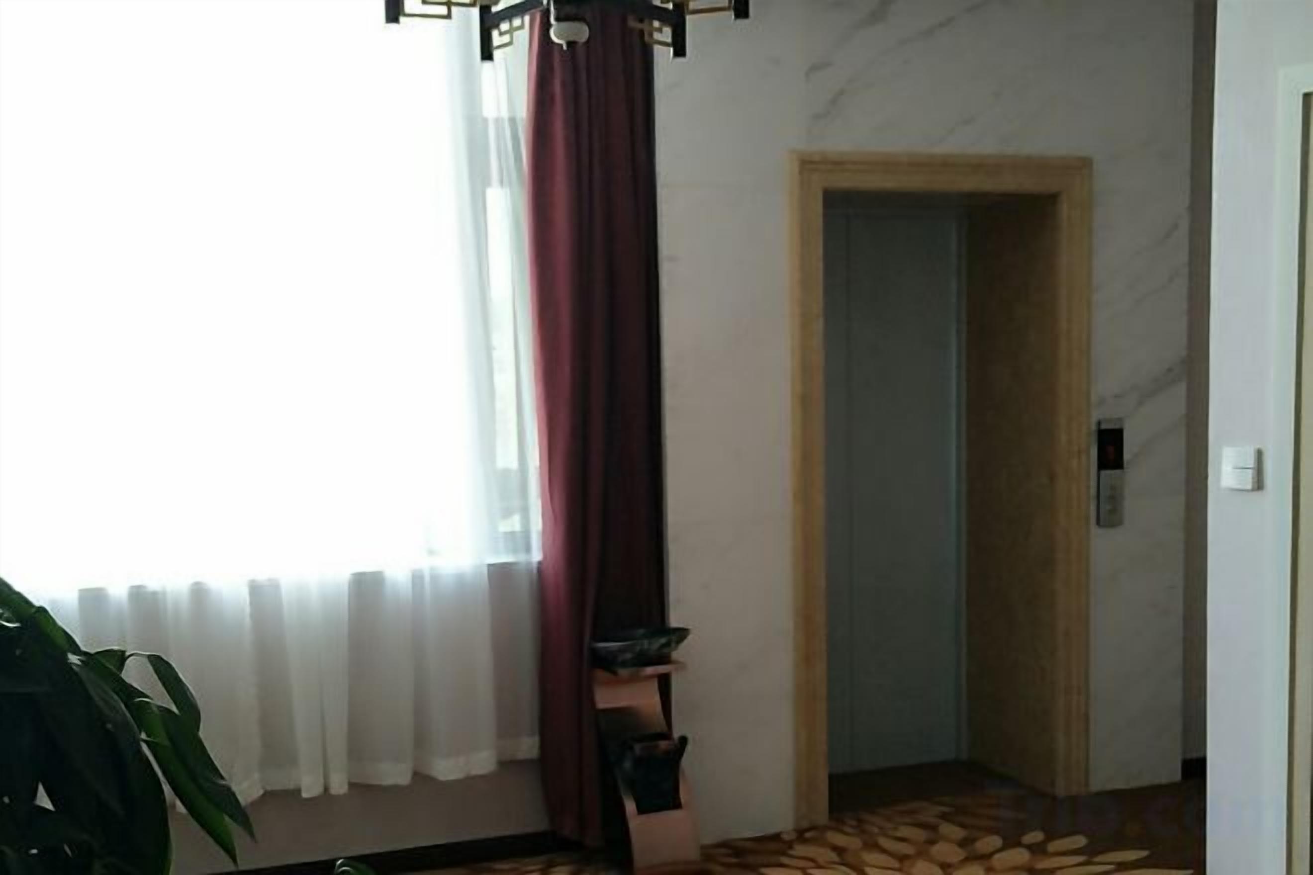 A room with a wooden door, a window with white curtains, and a floor with a patterned design.