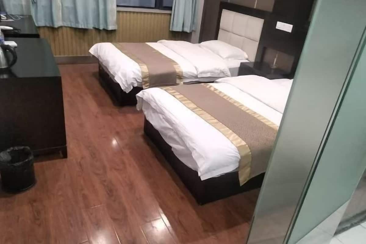 A hotel room with two beds, a desk, and a trash bin.