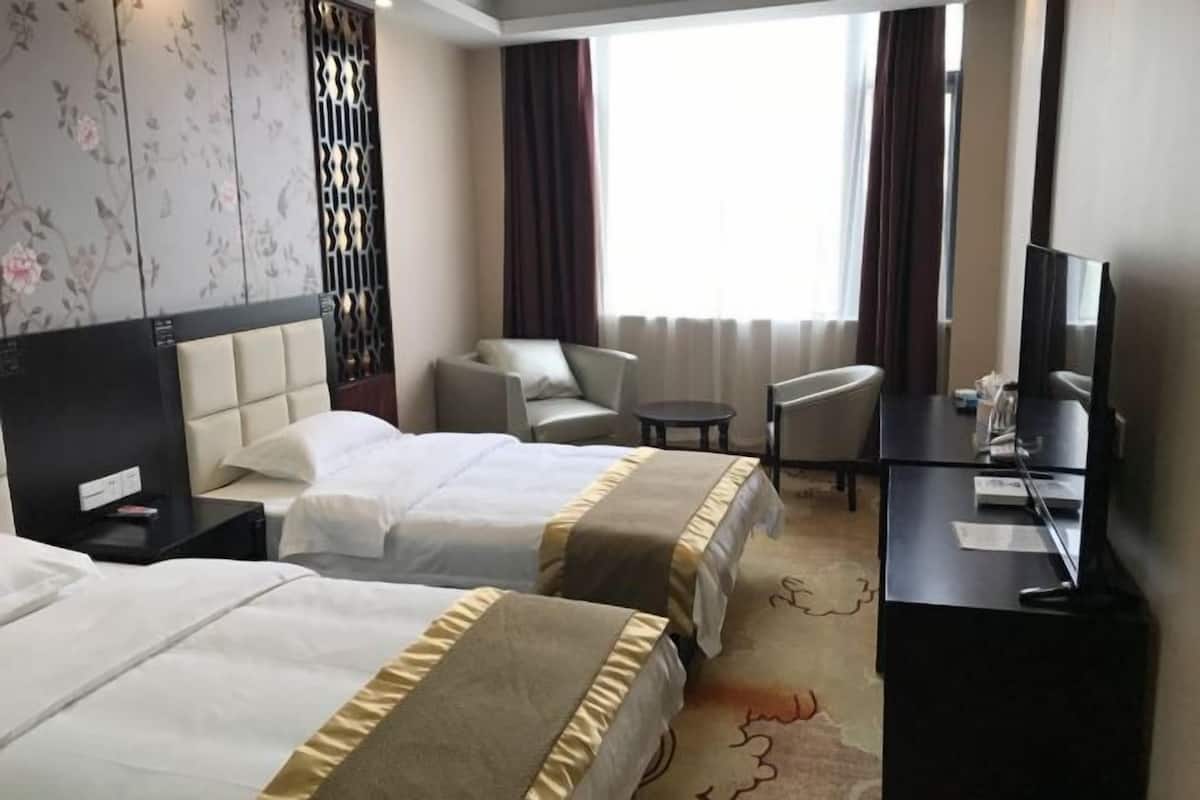 A hotel room with two beds, a desk, a TV, and a window with curtains.
